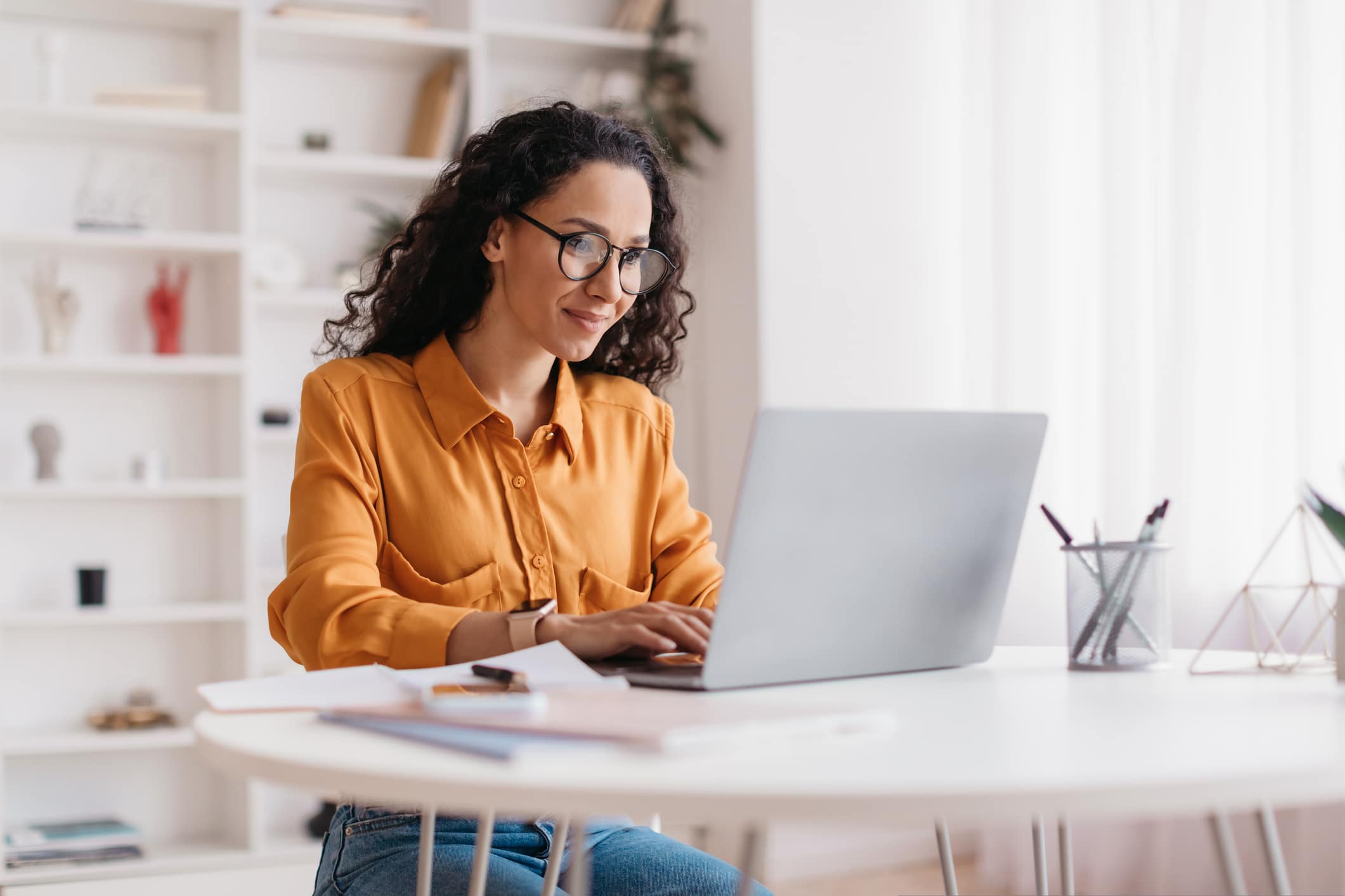 Middle Eastern Lady Using Laptop Working Online Wearing Eyewear Sitting At Workplace In Modern Office. Remote Job, Technology And Career Profession Concept. Side View