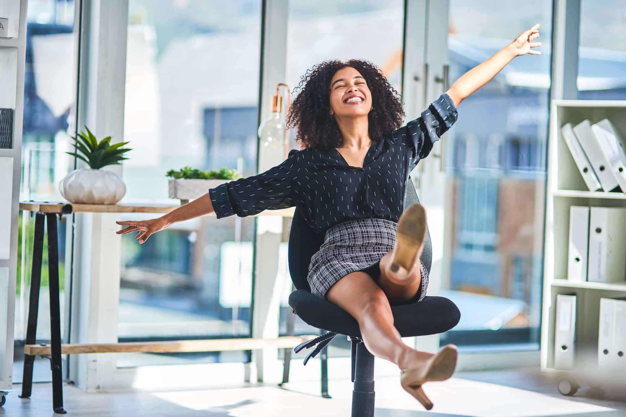 Full length shot of a young businesswoman sitting alone in her office and feeling playful during a break