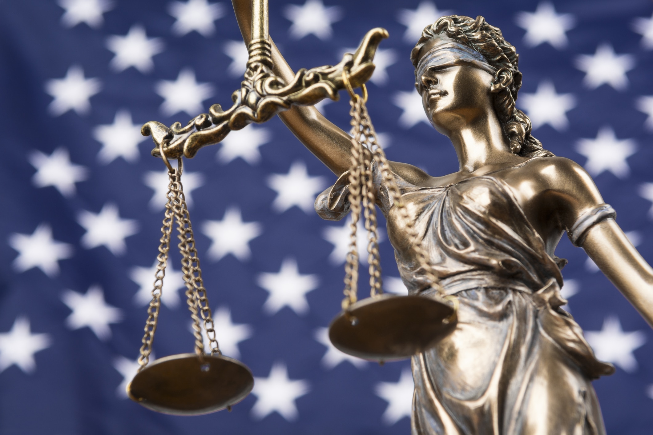 The statue of justice Themis or Justitia, the blindfolded goddess of justice against a flag of the United States of America, as a legal concept