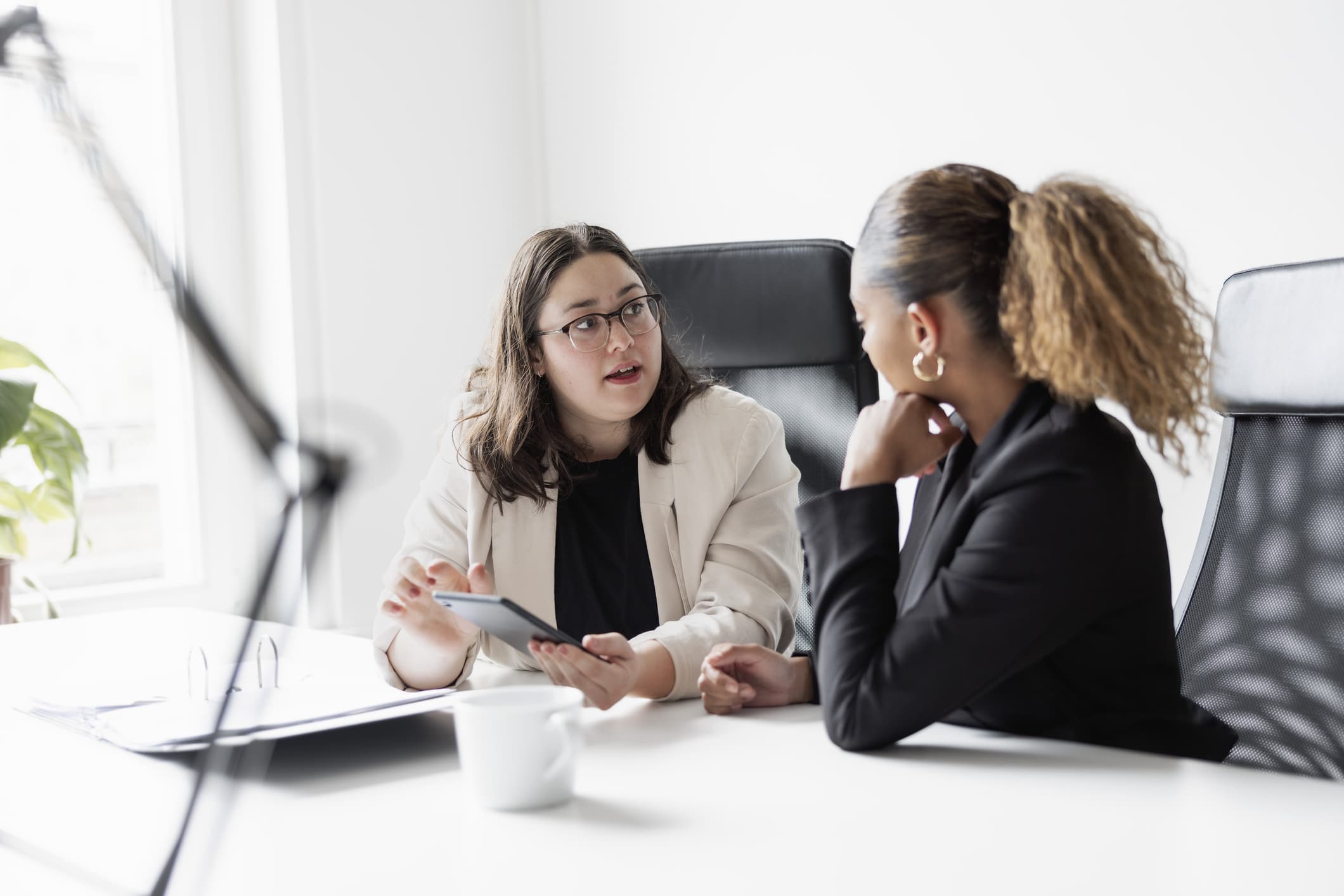 Two female coworkers discussing over digital tablet in office.