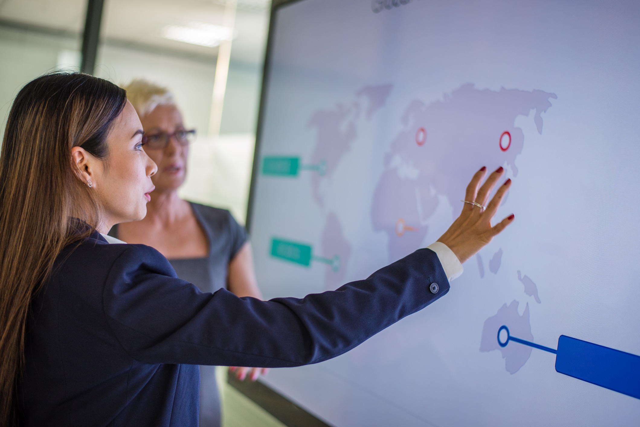 Businesswoman explaining global map to her coworker in conference room.