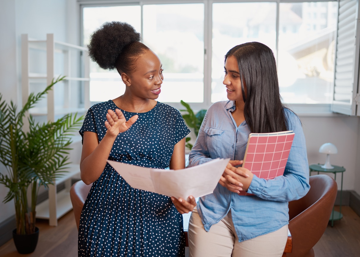 Two women discuss work solutions in boardroom office