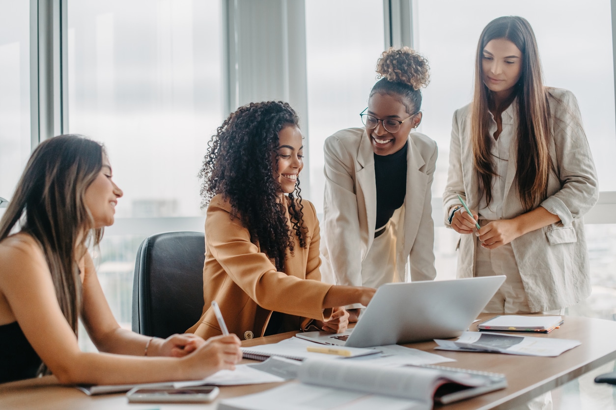 Four women gathered together in an office, discussing something during a meeting