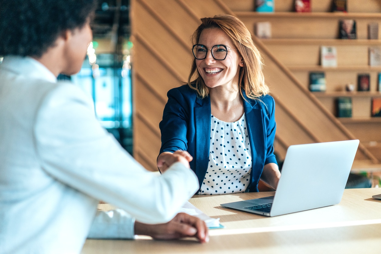 Two employees sitting a table and shaking hands in the office.