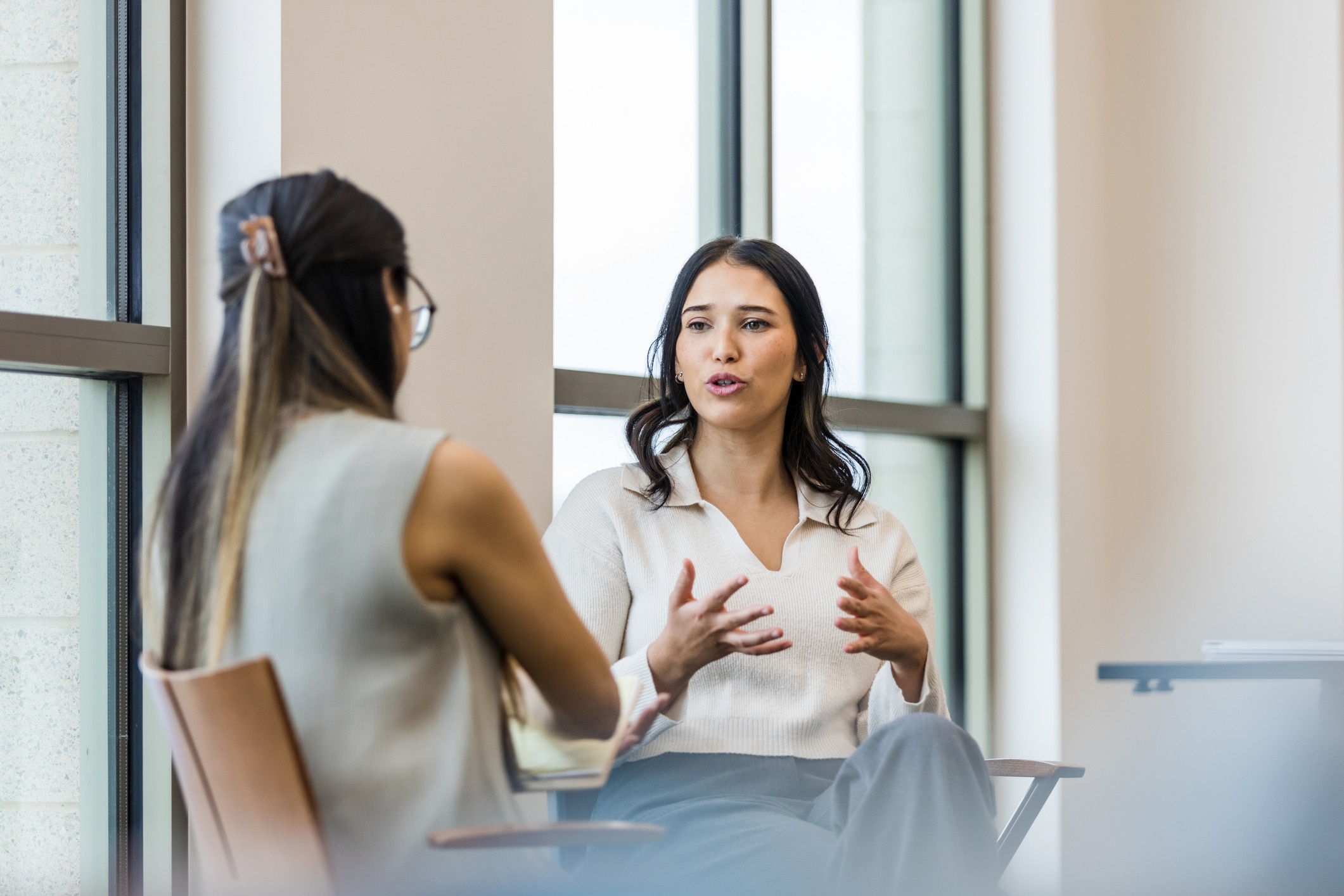 Two young adult women having a conversation while sitting down.