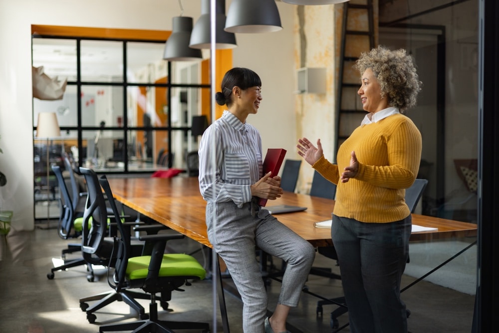 Happy businesswomen communicating while working in the office. The view is through glass.