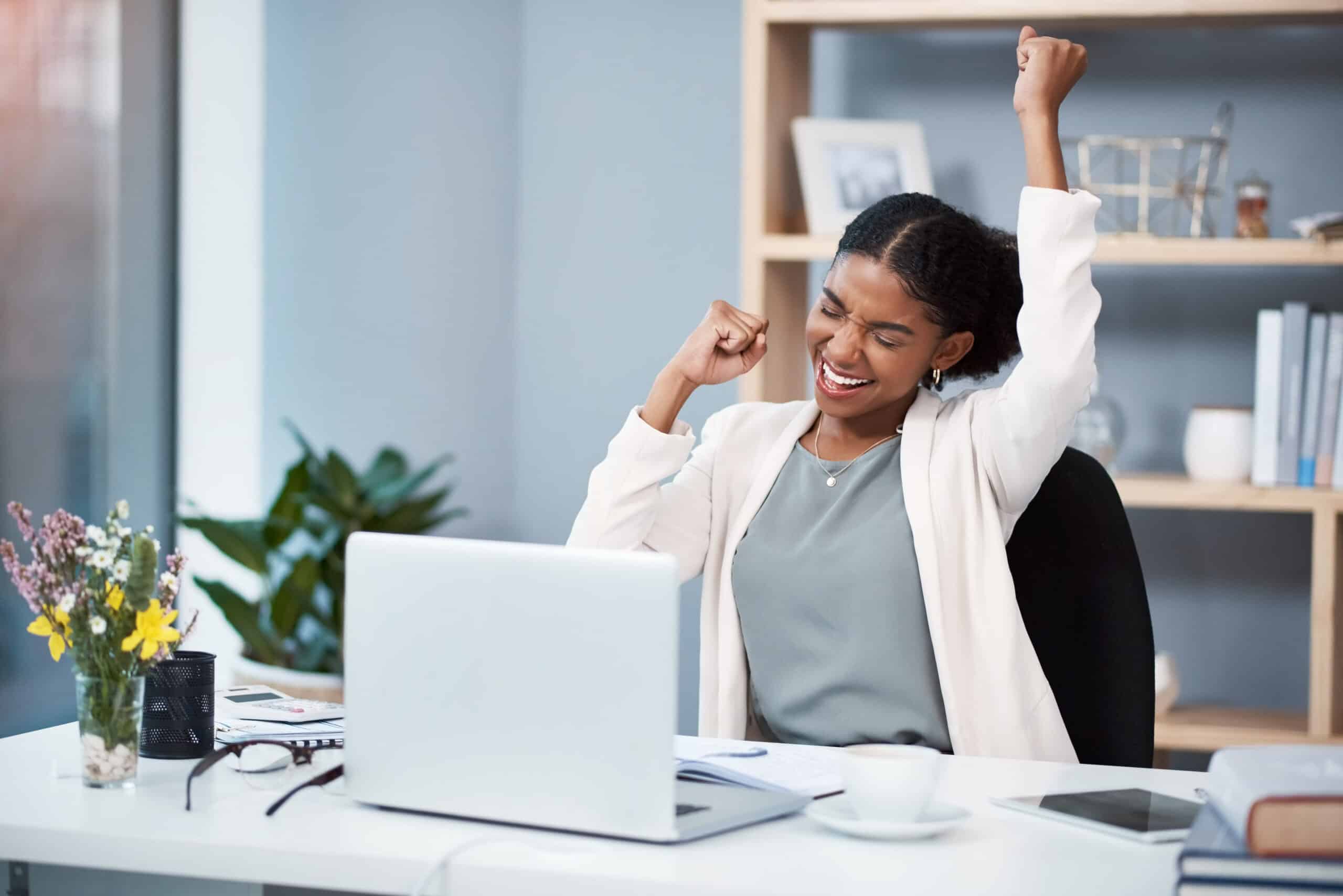 A happy young businesswoman celebrating at her desk in a modern office