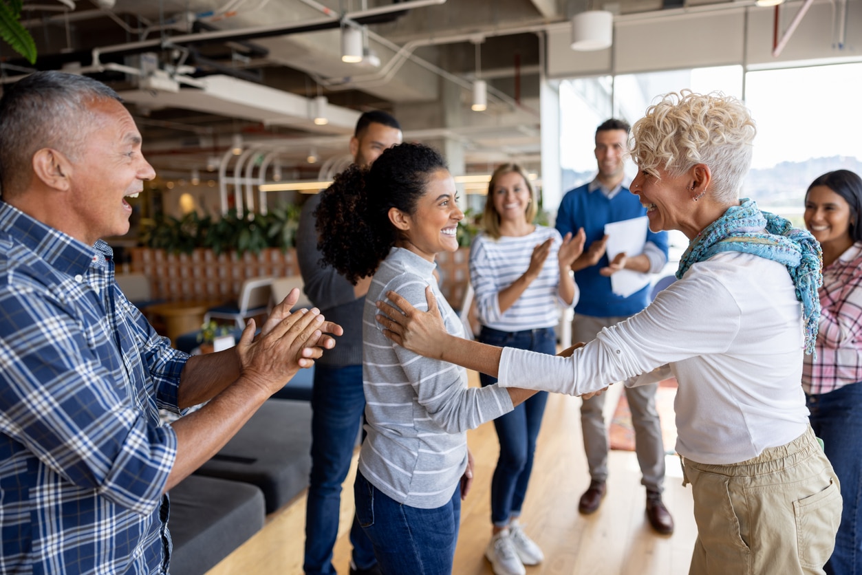 Boss giving woman a promotion at the office and team clapping for her