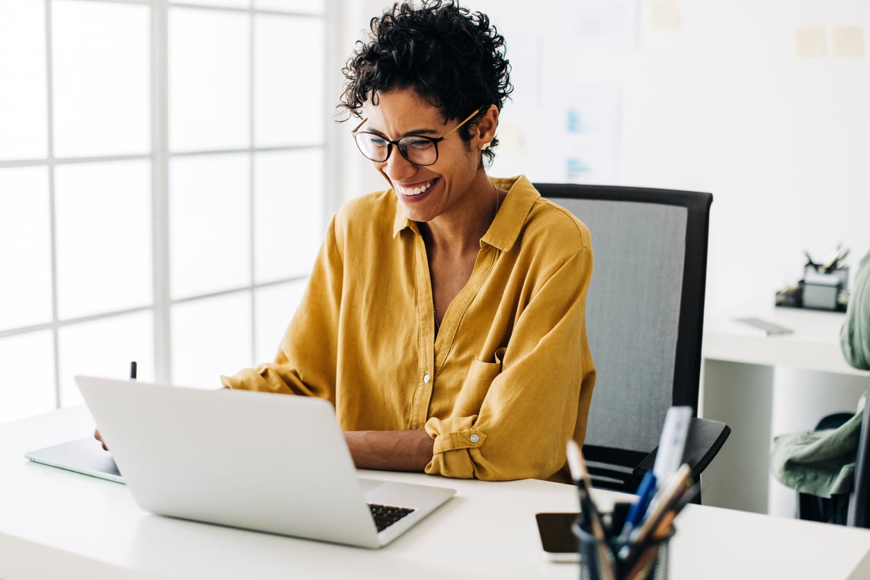 Woman smiles as she works on a laptop in an office.