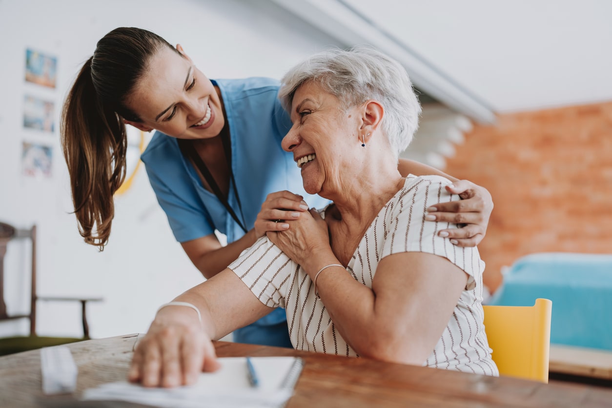 At-home healthcare professional hugging senior patient.