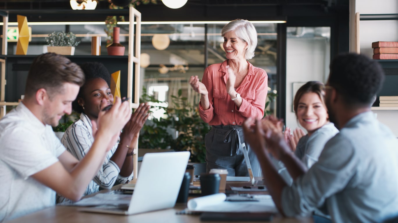 A group of businesspeople smiling and clapping during a meeting in the office.