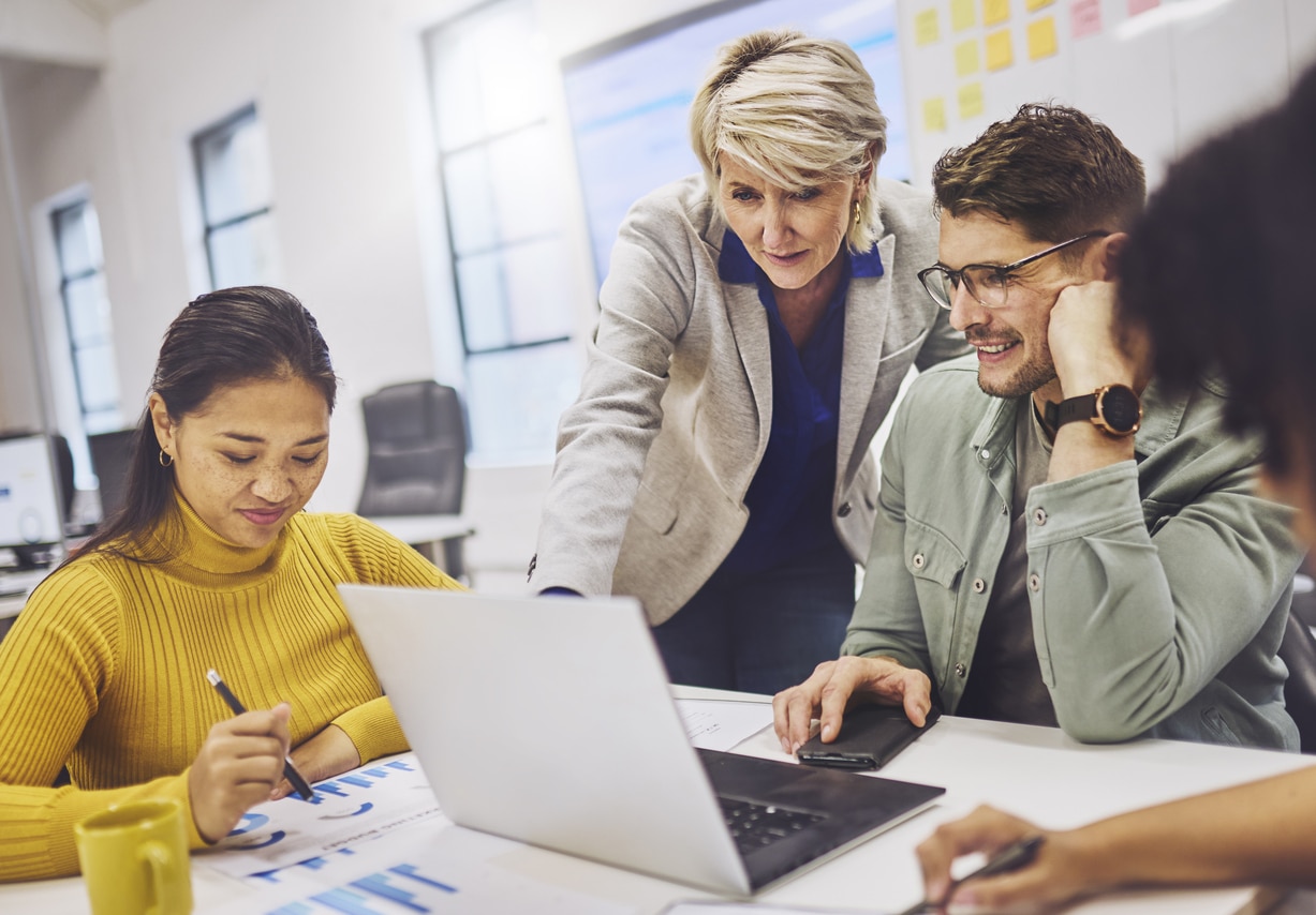 Senior female manager standing and pointing at a laptop while male employee observes during a meeting in the office.