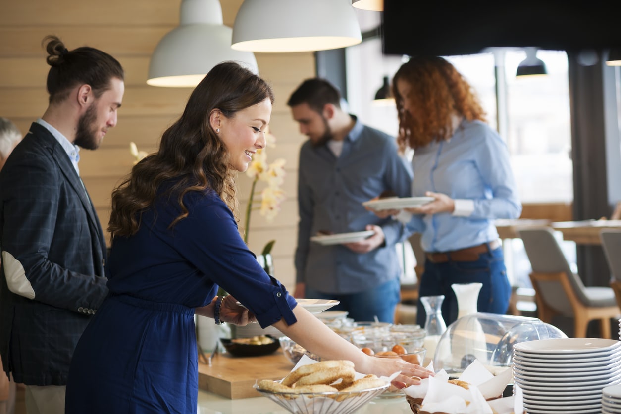 Coworkers choose food at a banquet-style lunch.