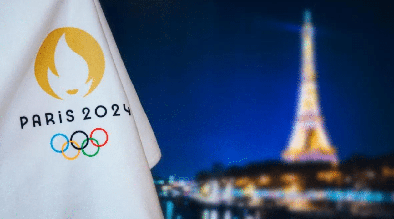 Paris 2024 olympics logo with eiffel tower at night blurred in the background