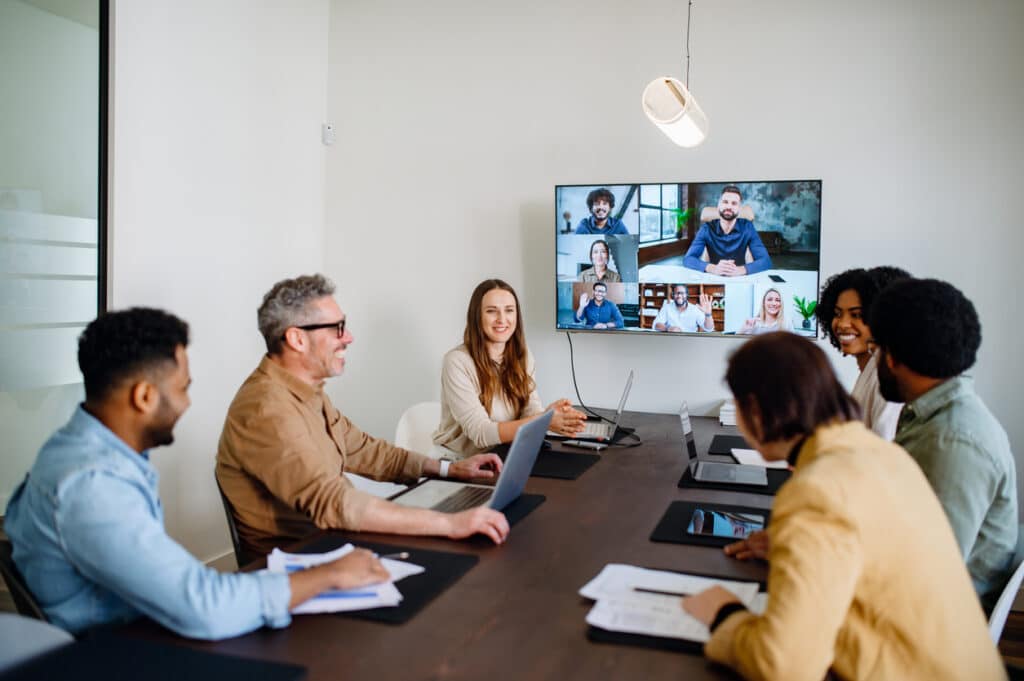 A lively and productive team meeting is captured where colleagues are connected via a large screen, showcasing a blend of in-person and remote collaboration.